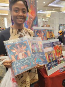 An African American young woman holding Black Fairy Coloring Book Black Mermaids Coloring Book by ND Jones